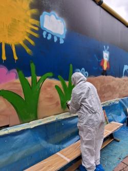 Nuori maalaamassa graffitia valkoisessa suojahaalarissa.