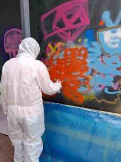 Nuori maalaamassa graffitia valkoisessa suojahaalarissa.